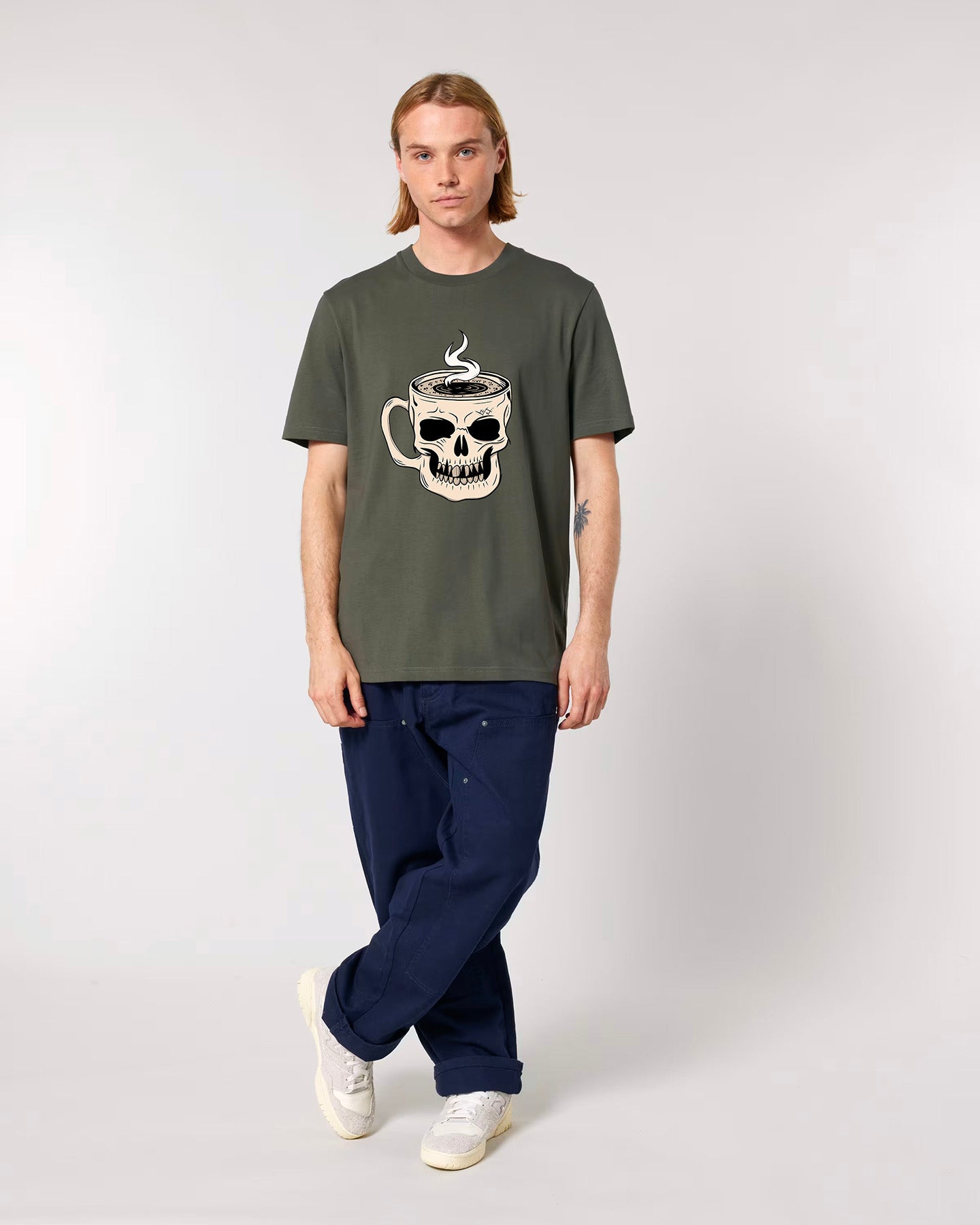 Person wearing a green t-shirt with a skull and coffee cup design on a plain background