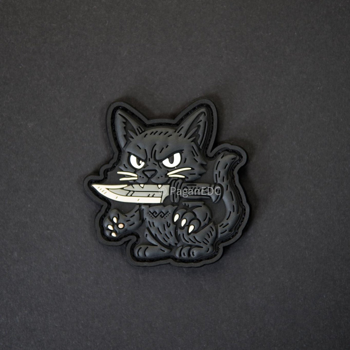 PVC patch featuring a black cat holding a knife, designed by PaganEDC, with glow-in-the-dark eyes and 3D detailing on a black background.