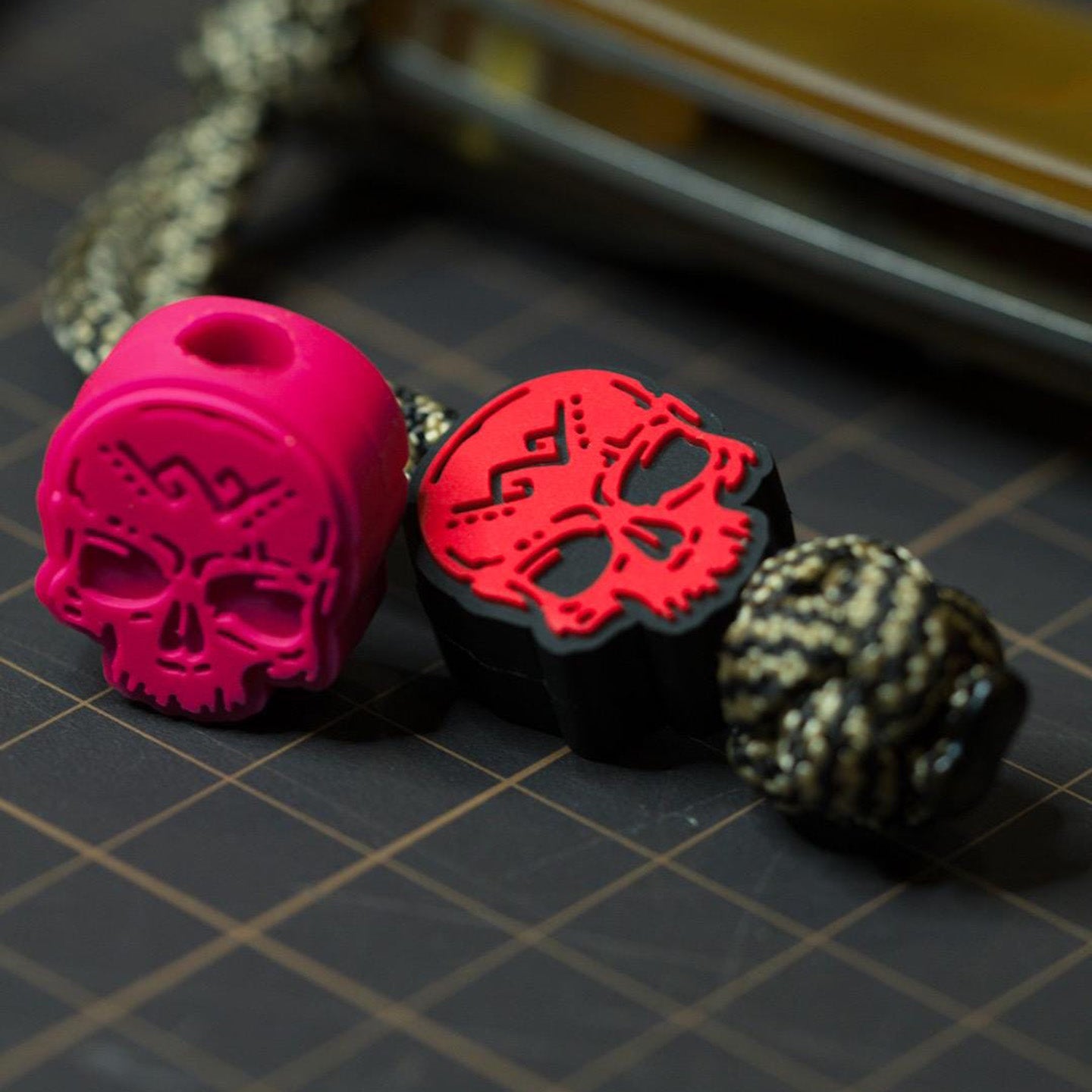 PVC pagan skull bead in pink and red attached to a paracord lanyard, shown as an EDC accessory on a cutting mat background.