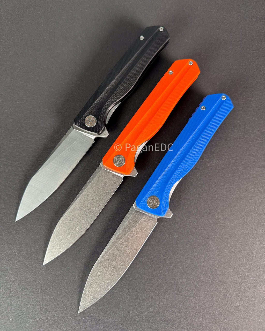 Three folding knives with black, orange, and blue handles on a gray background.