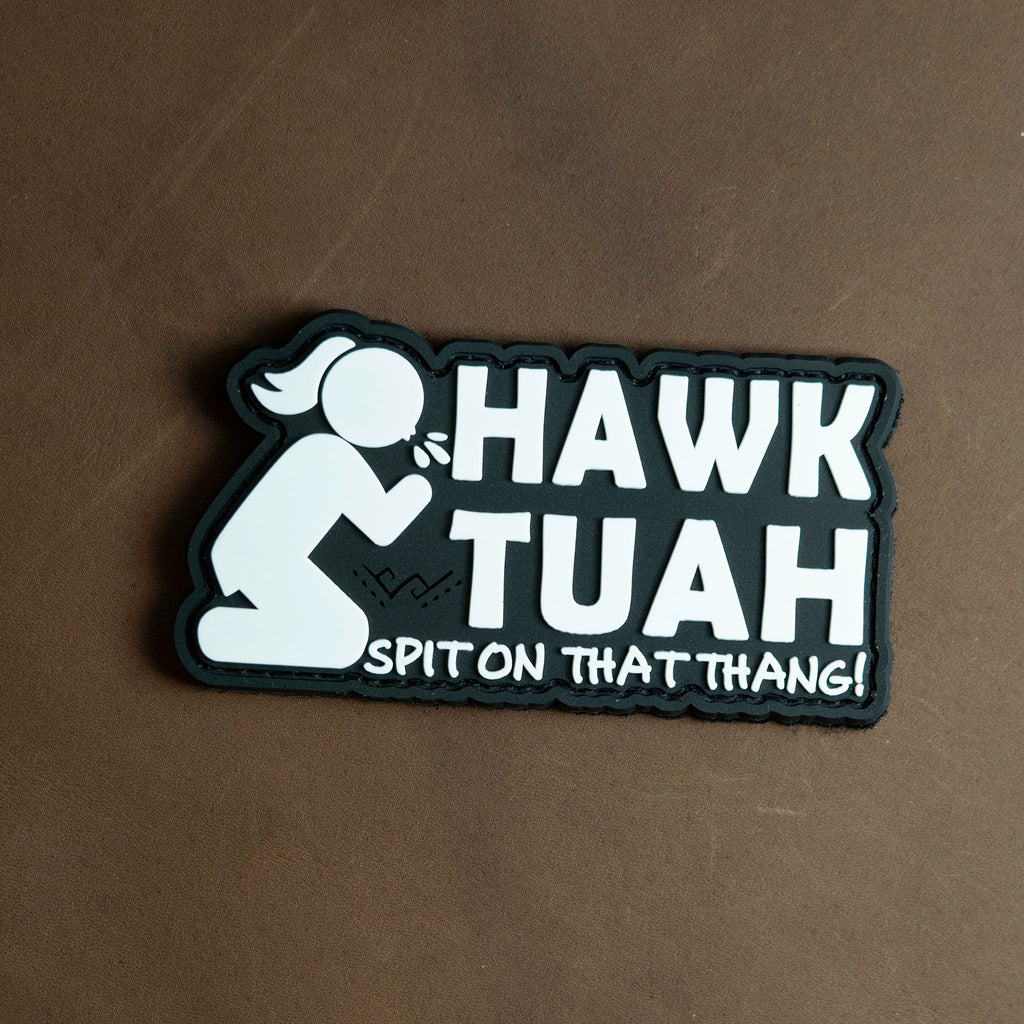 Black and white PVC patch featuring the phrase “Hawk Tuah – Spit On That Thang!” with a kneeling cartoon figure.