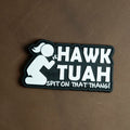 Black and white PVC patch featuring the phrase “Hawk Tuah – Spit On That Thang!” with a kneeling cartoon figure.
