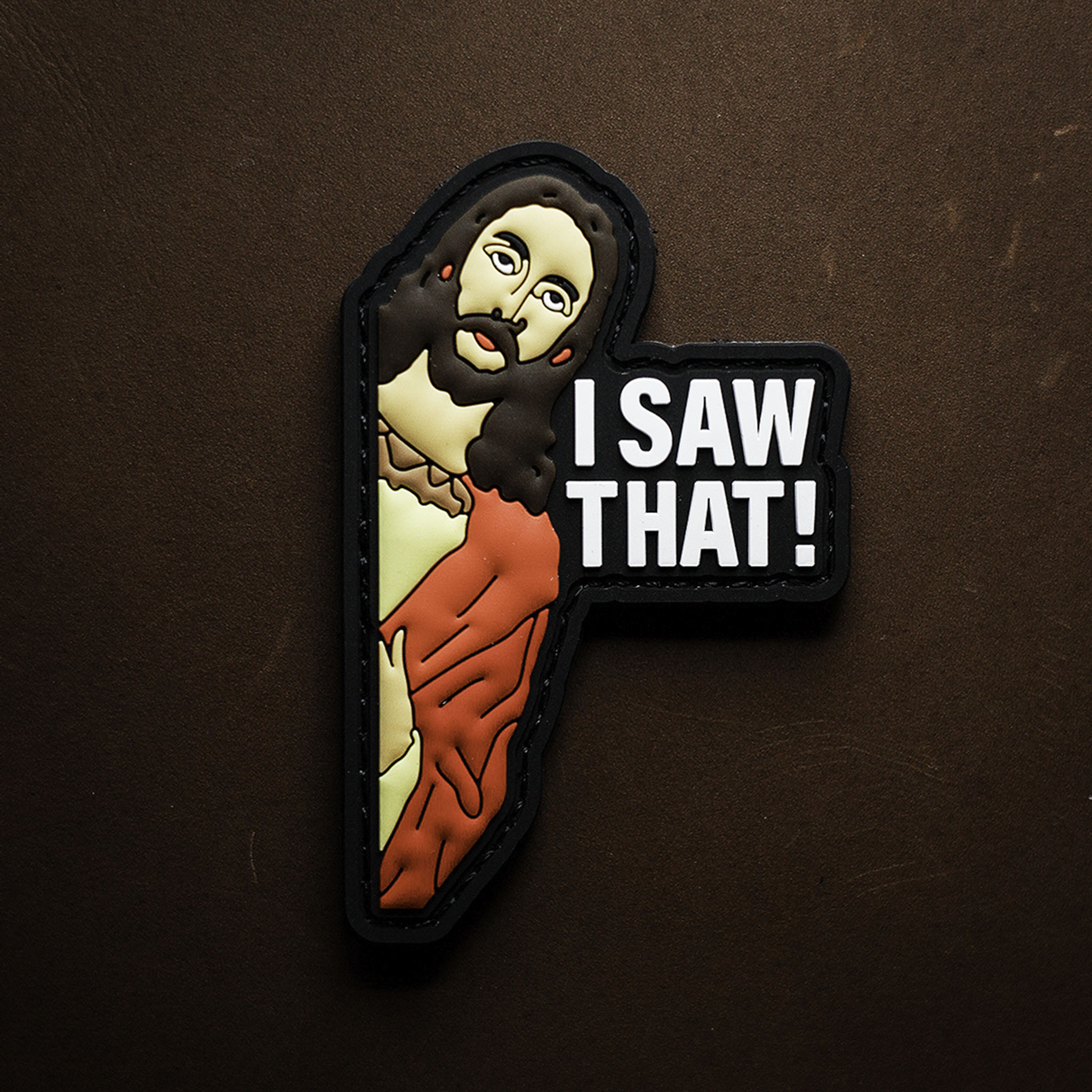 PVC patch showing a stylized religious figure peeking with the words “I SAW THAT!” on a black background.