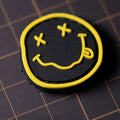Black and yellow PVC patch with a smiley face featuring crossed eyes and a tongue-out design.