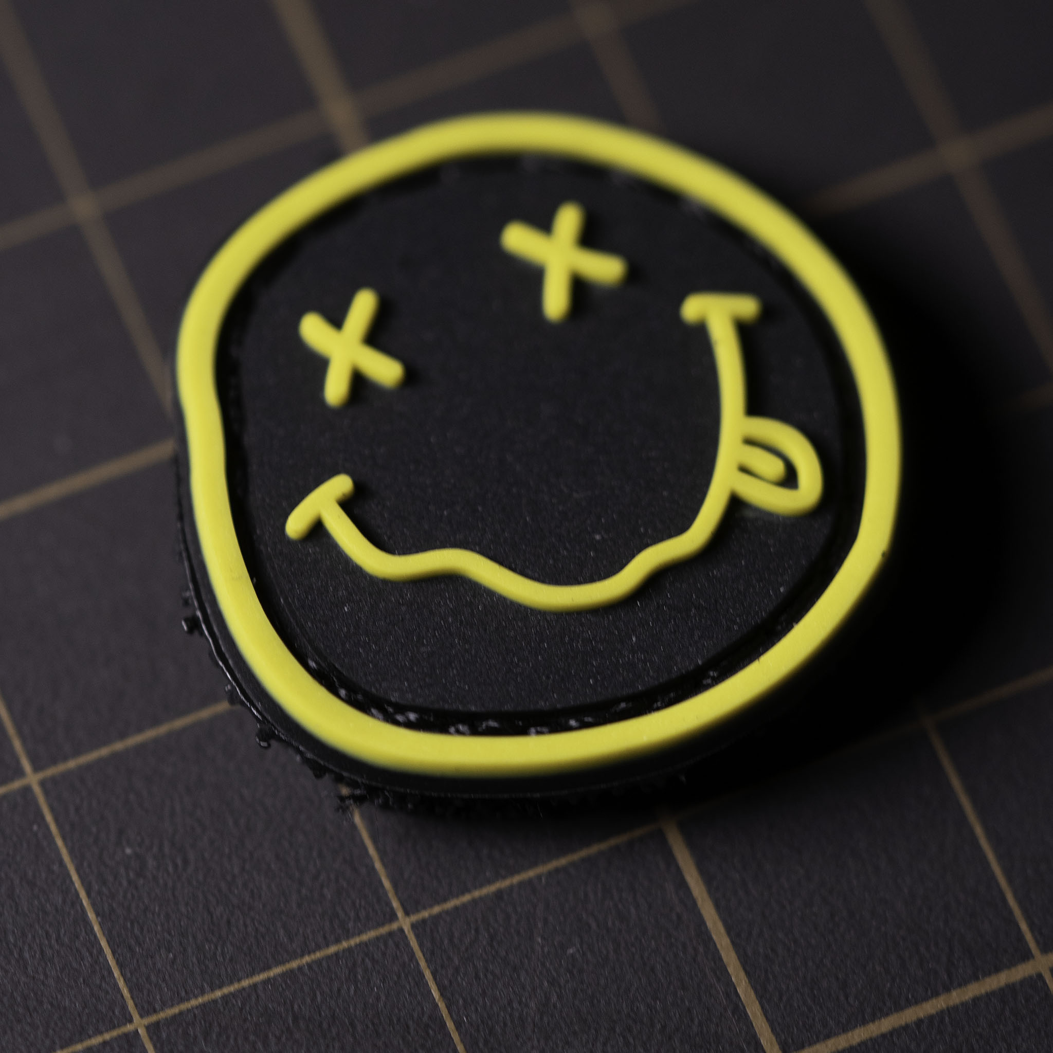 Black and yellow PVC patch with a smiley face featuring crossed eyes and a tongue-out design.