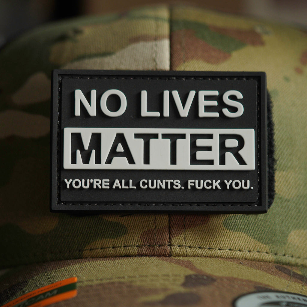 Black PVC patch with raised white text reading ‘NO LIVES MATTER’ and an additional offensive line of text, attached to a camouflage cap.