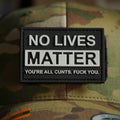 Black PVC patch with raised white text reading ‘NO LIVES MATTER’ and an additional offensive line of text, attached to a camouflage cap.
