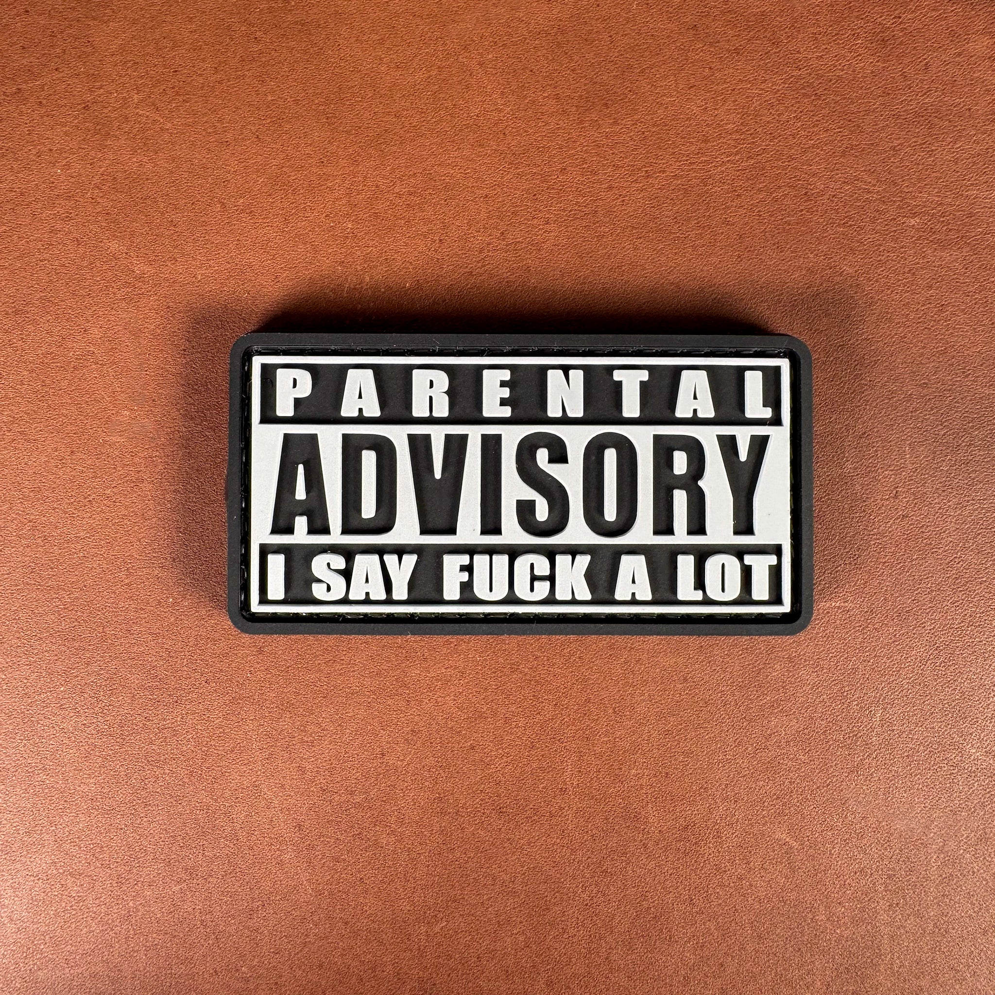 “Parental Advice” black and gray PVC patch on brown background