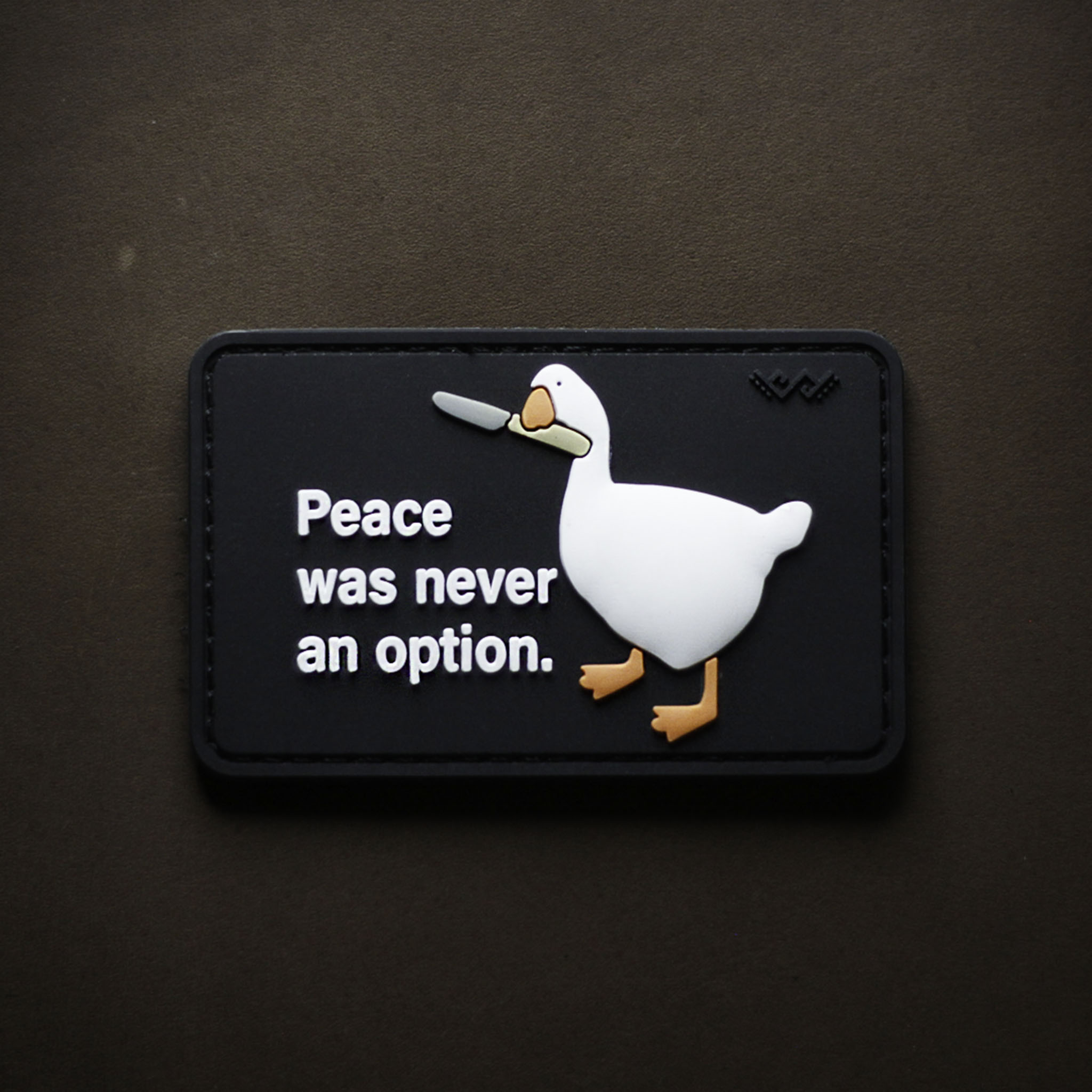 PVC patch with a white goose holding a knife and the text ‘Peace was never an option’ on a rectangular background.