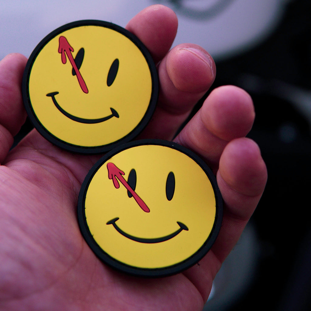 PVC Watchmen smiley patch with blood splatter held in a hand.