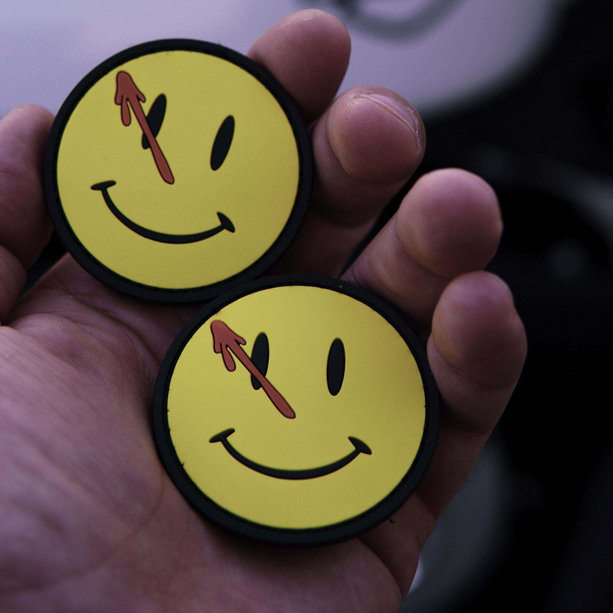 PVC Watchmen smiley patch with blood splatter held in a hand.